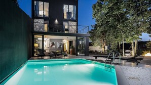 A modern two-story house with a swimming pool, outdoor seating, and a balcony.
