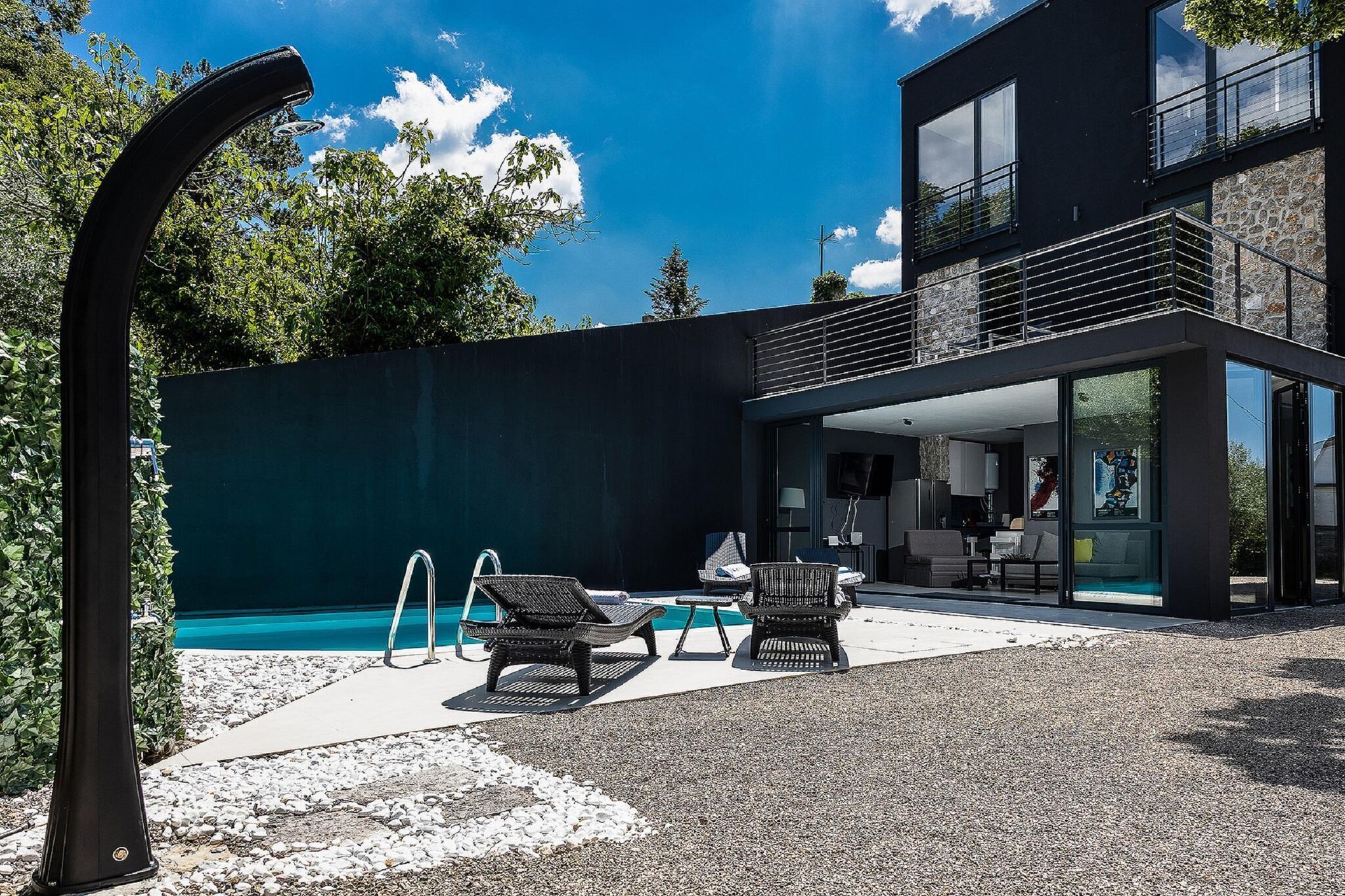 Un espace piscine extérieur moderne, doté de chaises longues et d’un coin salon abrité.