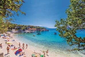 A beach with clear turquoise water, people sunbathing, and boats docked near the shore.