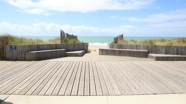 A wooden boardwalk leading to a beach with a clear sky.