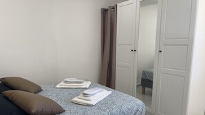 Un lit bien fait, recouvert d’une couvre-lit à motifs, avec deux oreillers et des serviettes pliées. On y trouve également une armoire avec un miroir et une porte.