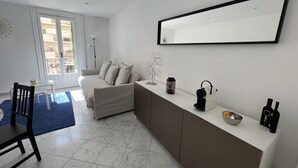 Un salon moderne comprenant un canapé, une table à manger avec des chaises, un coin cuisine avec un comptoir et un grand miroir au mur.