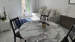 Un salon moderne avec une table à manger en marbre, un canapé et un balcon doté de volets verts.