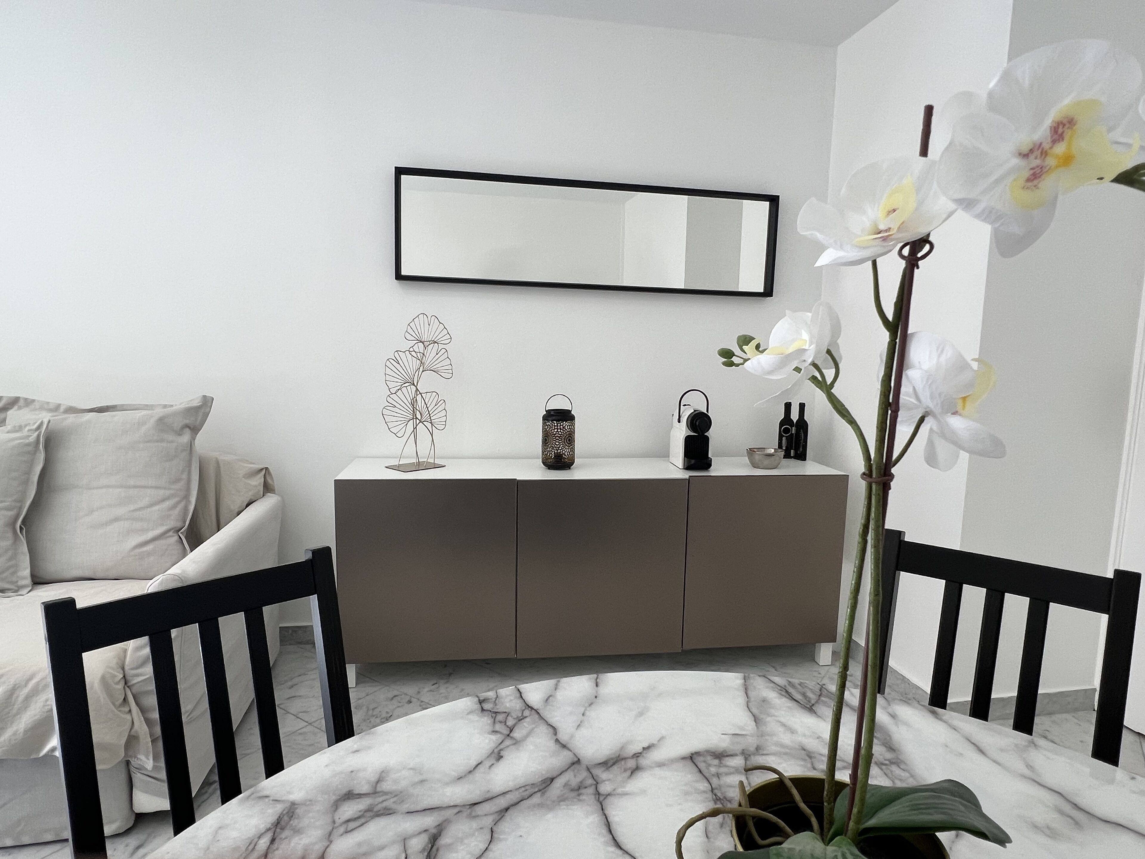 A modern room with a marble floor, a white sofa, a grey cabinet, and a large mirror.