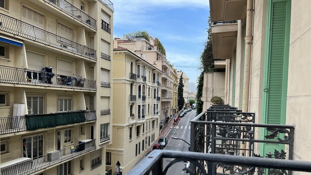Un immeuble à plusieurs étages doté de balcons, donnant sur la rue, avec un pont en arrière-plan.
