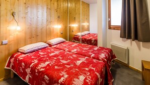 A room with wooden panel walls, two beds with red bedding, a large mirror, and a window with curtains. - Modern 4-room apartment, 2 terraces, covered parking, ski-in/ski-out (La Plagne Montchavin Les Coches)