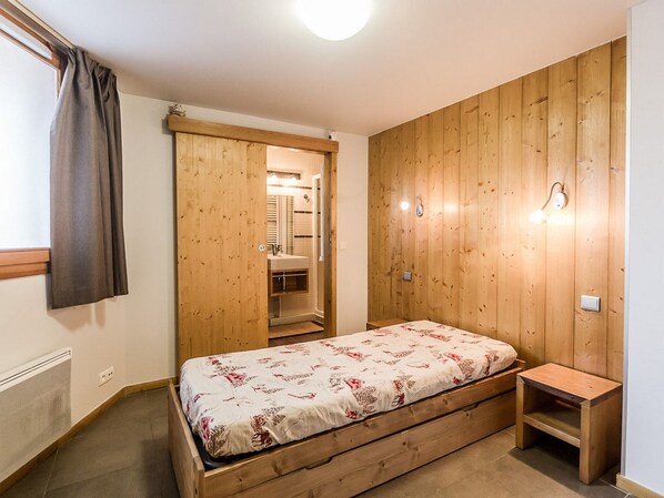A bedroom with a wooden bed, a small bedside table, a wardrobe, and a bathroom visible through an open door.