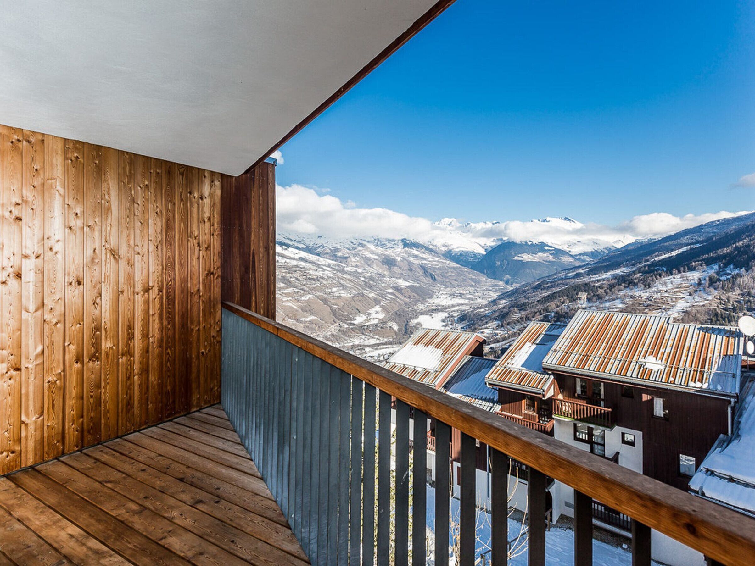 A wooden balcony with a view of snow-covered mountains and a valley.