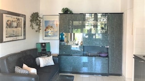 Et moderne køkken med glasvæg, en mørk sofa med mønstrede puder og et billede i ramme på væggen.