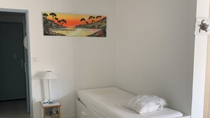 Een slaapkamer met een eenpersoonsbed, een klein nachtkastje met een lamp, en een schilderij aan de muur.
