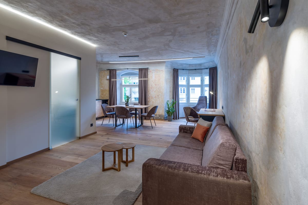 A modern living room with a sofa, chairs, a table, and a TV.