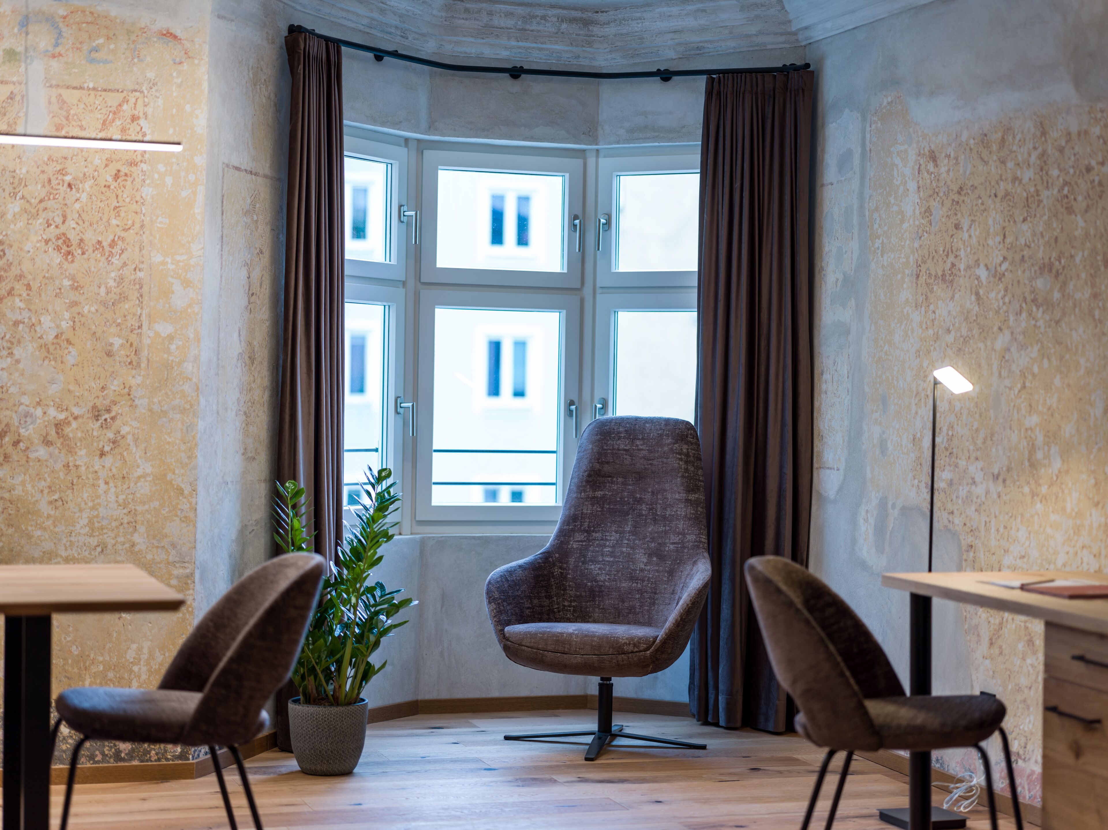 A corner room with a large window, two chairs, a table, and a potted plant.