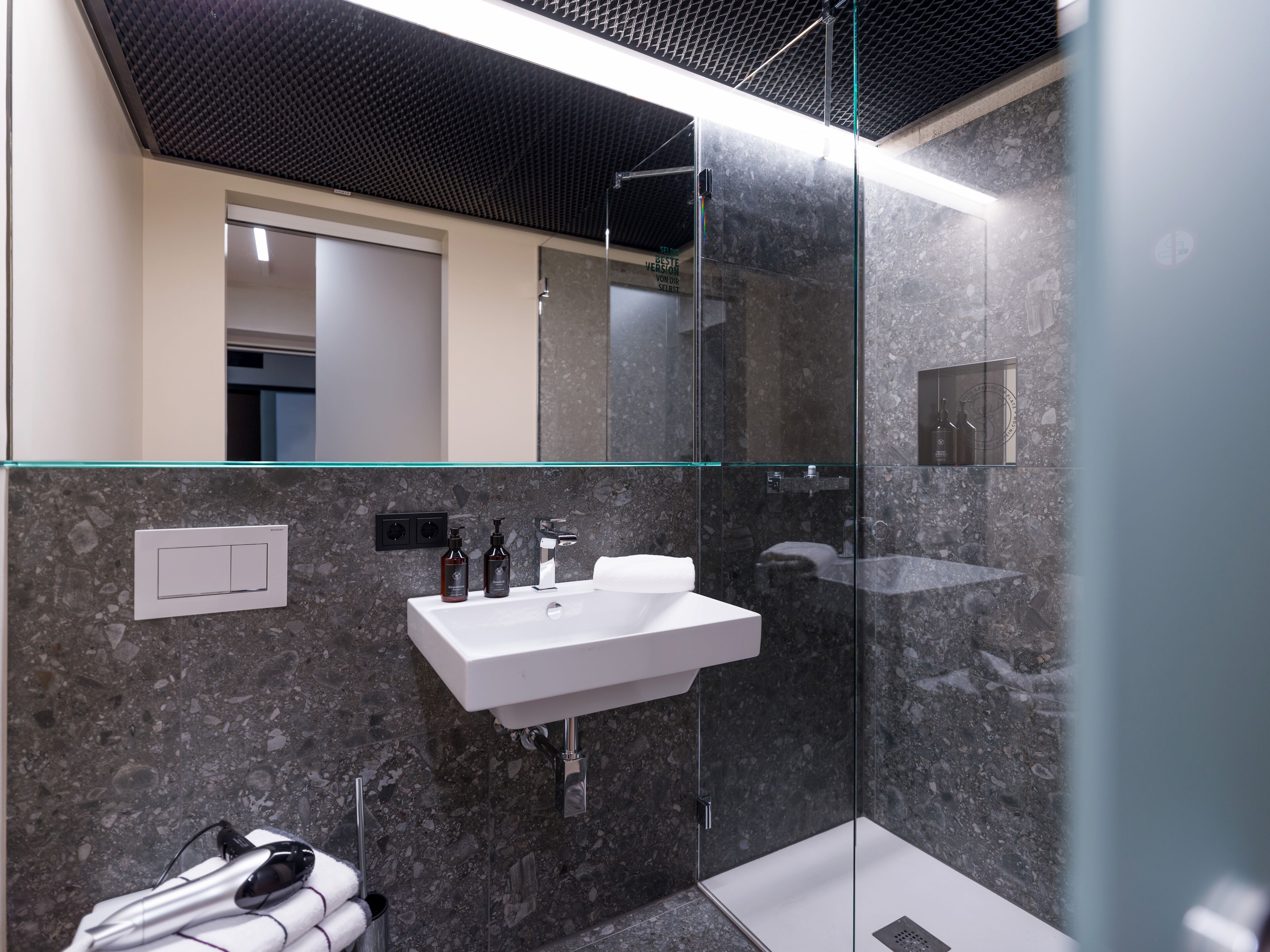 A modern bathroom with a glass shower enclosure, a white sink, and a marble wall.