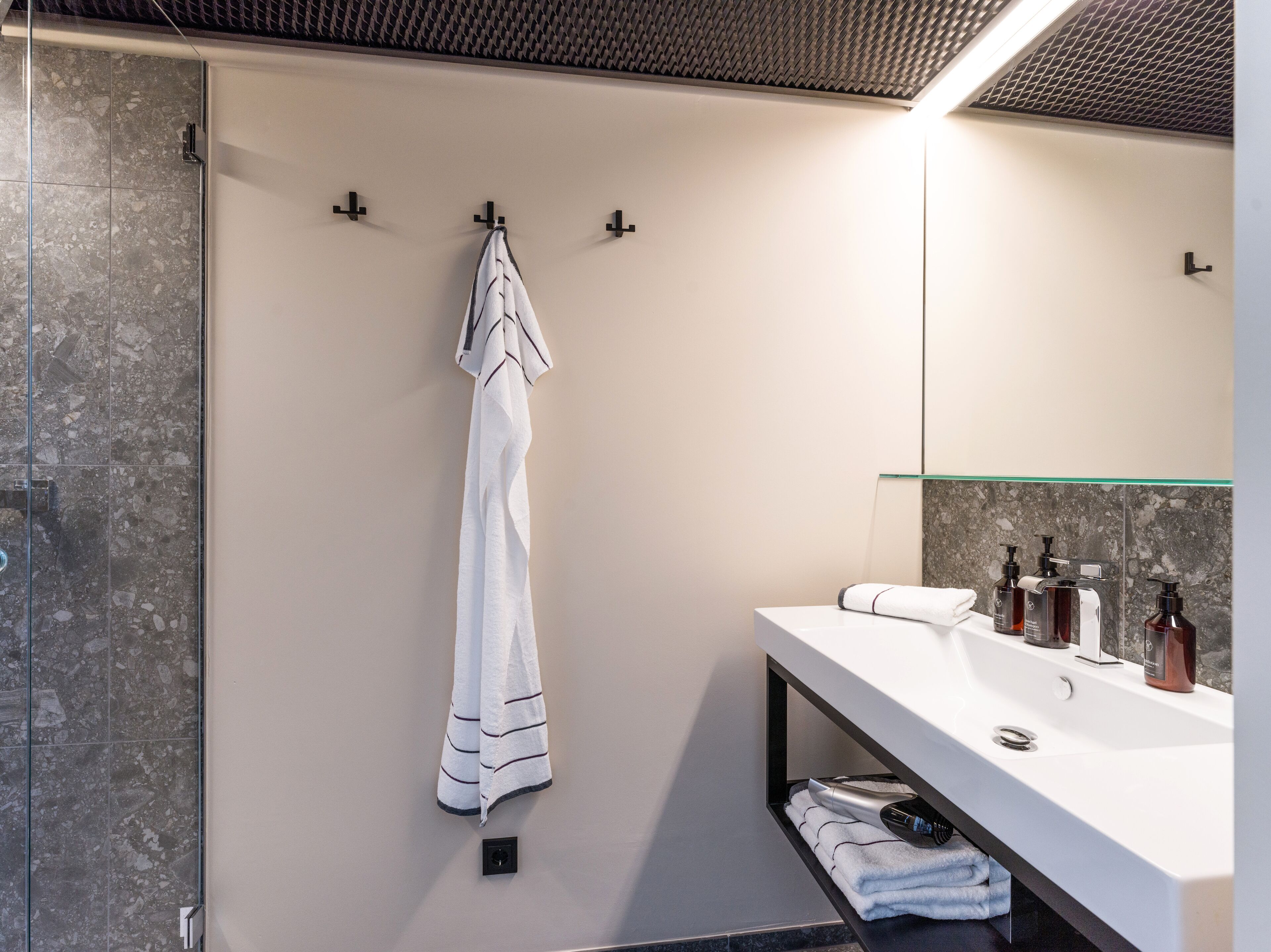 A modern bathroom with a glass shower enclosure, a white towel hanging on a hook, and a white sink with toiletries.