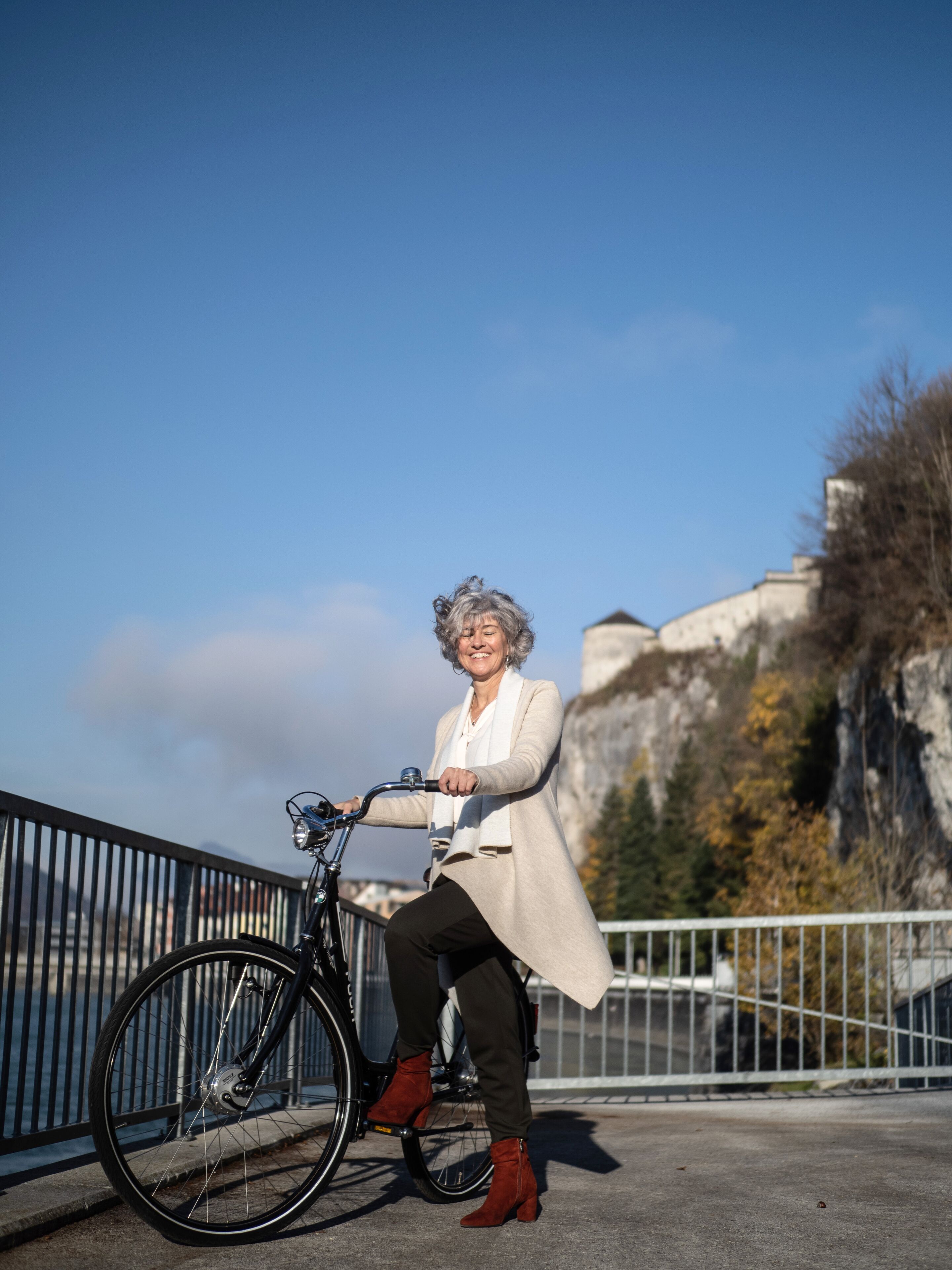 A person sitting on a bicycle on a bridge with a mountainous backdrop.