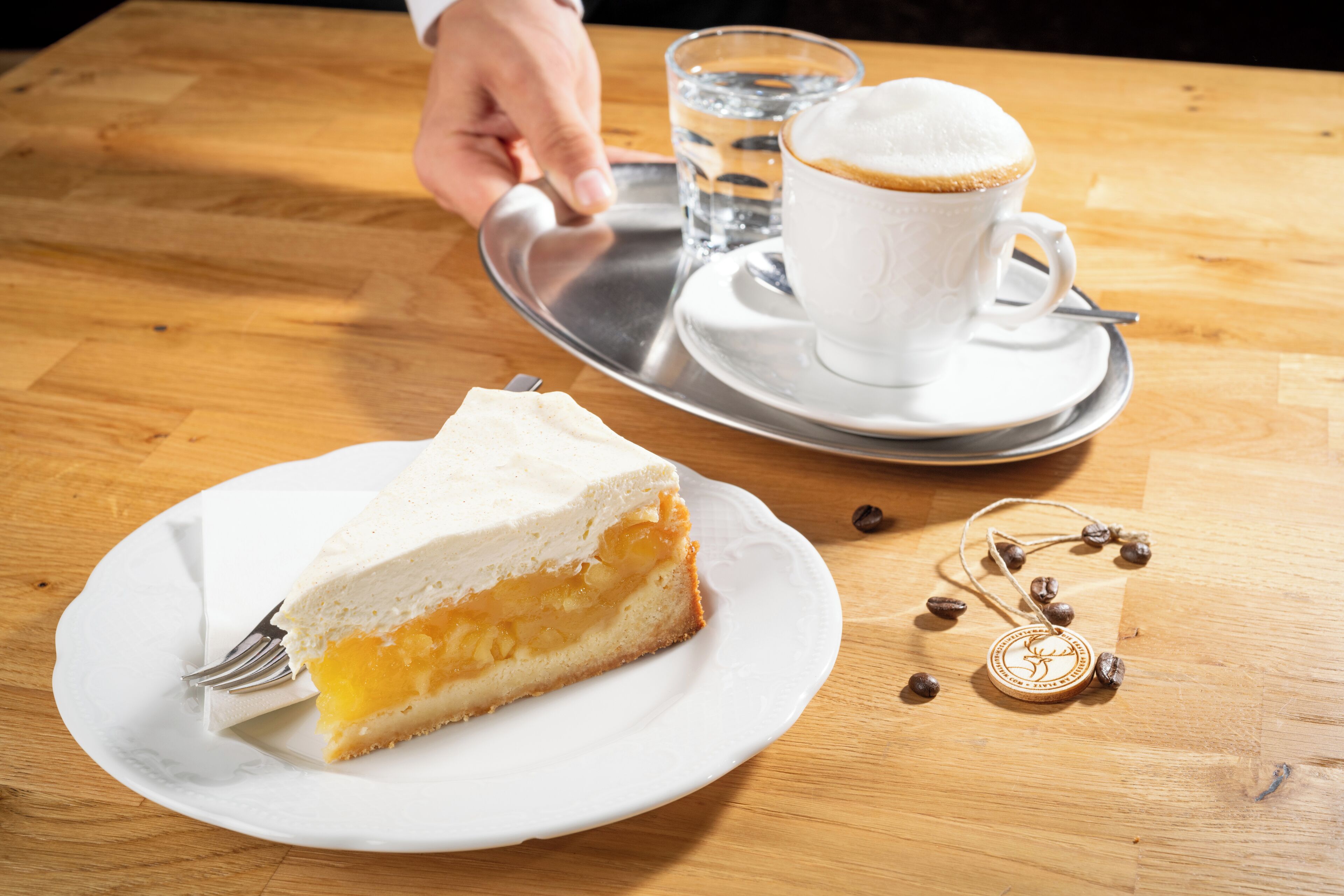 Een plakje taart op een bord, een kop koffie, en een dienblad met een glas water.