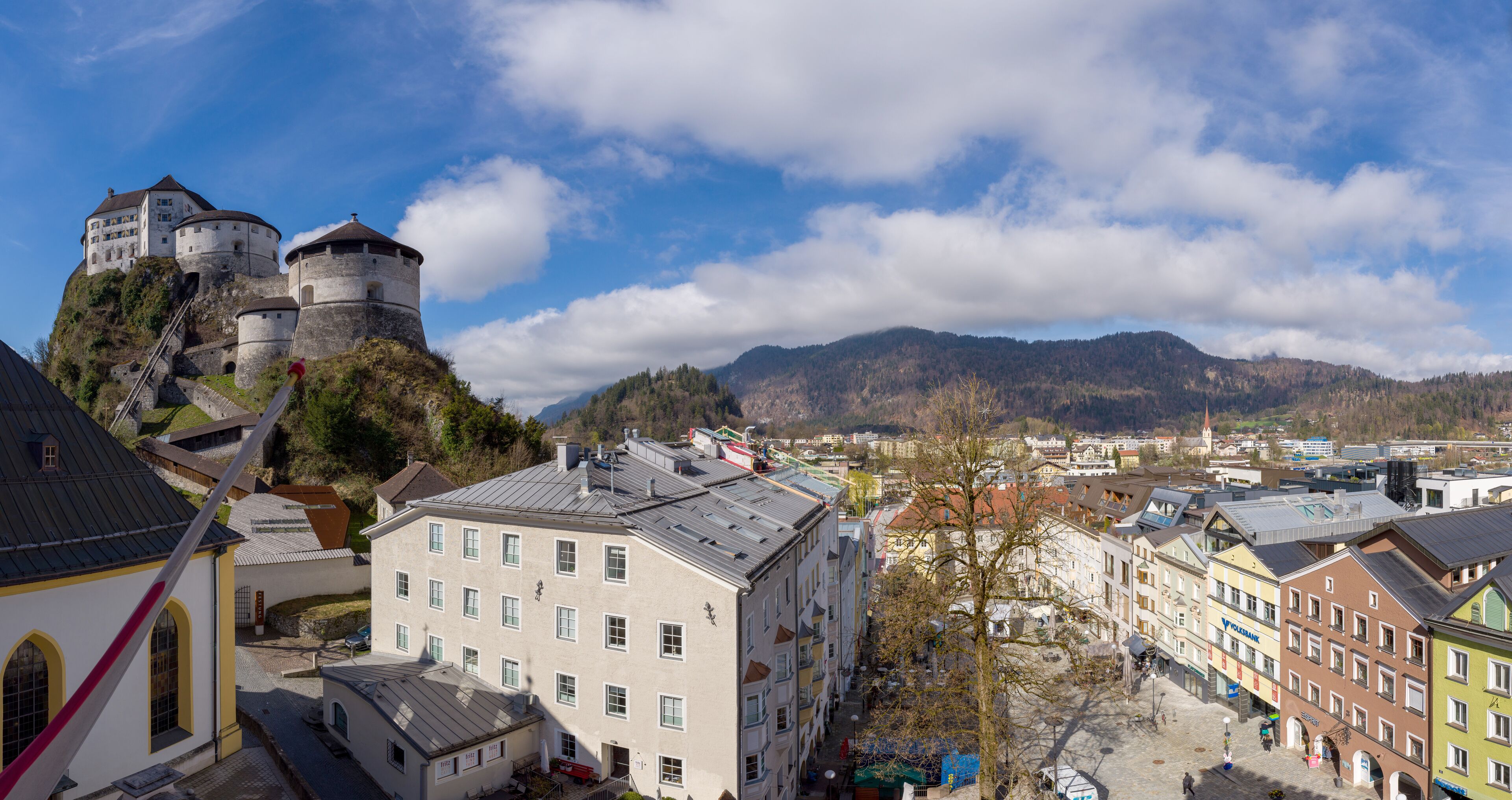A historic castle on a hill overlooking a town with colorful buildings and a clear sky.