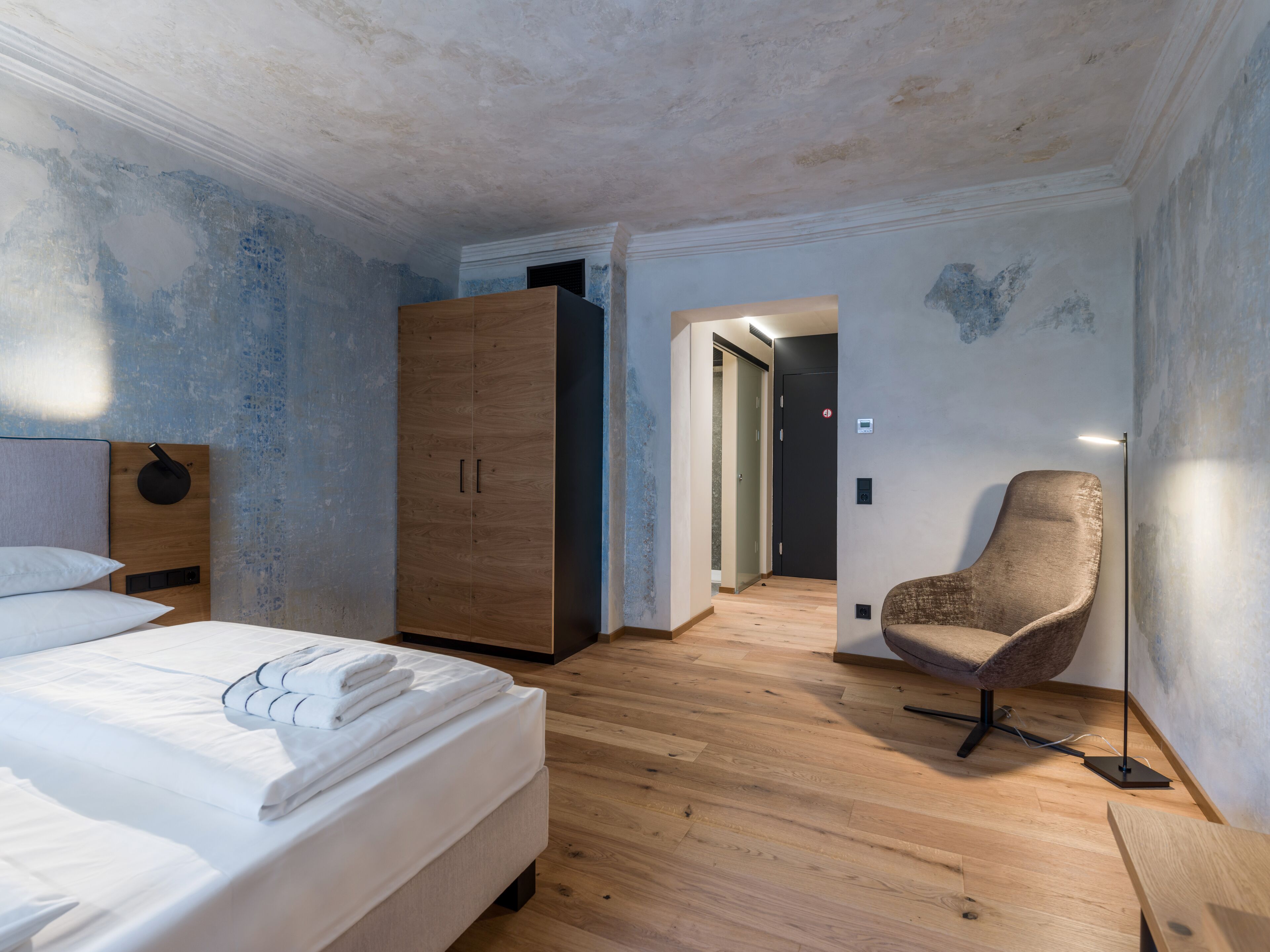 Un dormitorio con un armario de madera, una silla y una cama con ropa de cama blanca impecable.