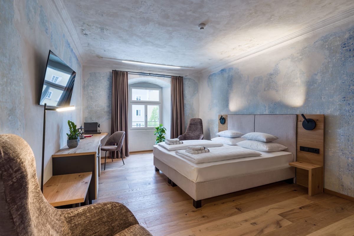 A modern bedroom with a large bed, a desk, a chair, and a TV mounted on the wall.
