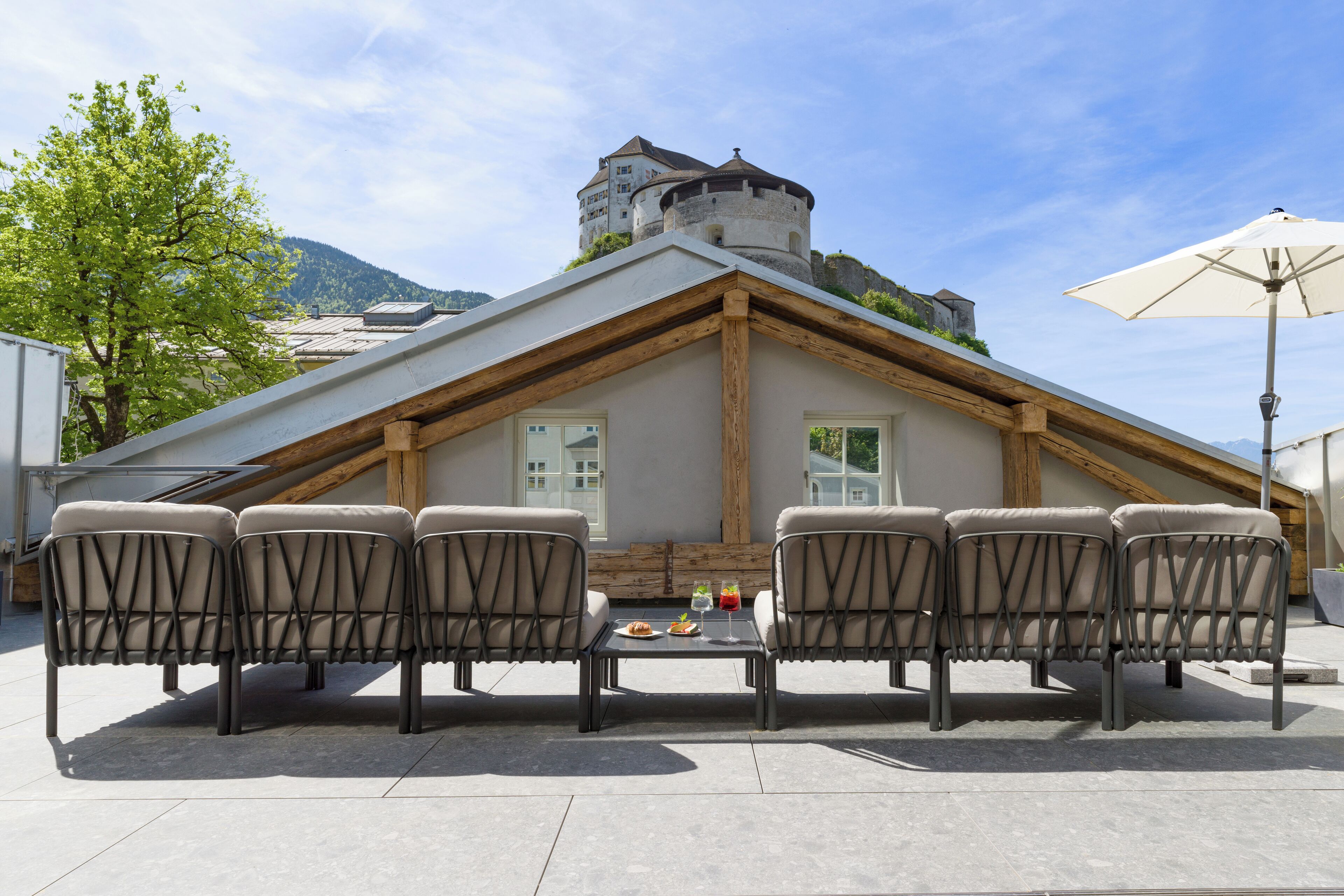 Eine Dachterrasse mit Essbereich, einem Tisch für vier Personen und sechs Stühlen, mit Blick auf ein schlossartiges Gebäude.