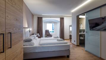 Una habitación de hotel moderna con una cama grande, una silla, un televisor y un baño visible a través de una puerta abierta.