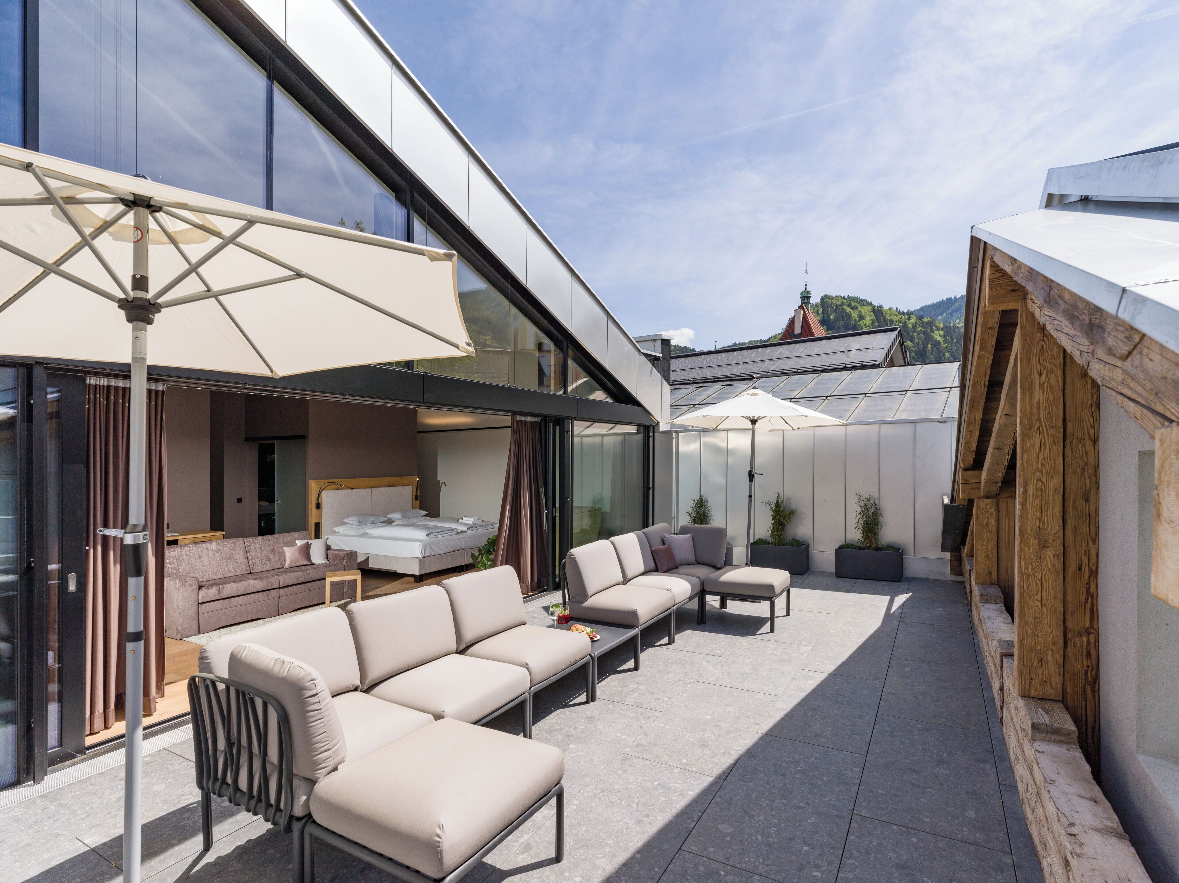 A modern outdoor living area with a sofa set, a dining table, and umbrellas providing shade.