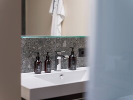 Un baño con un lavamanos blanco, una mampara de cristal y tres botellas marrón oscuro de champú.