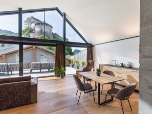 A modern interior with a wooden dining table, chairs, and a large window overlooking a castle. - Platzhirsch Kufstein (Kufstein)