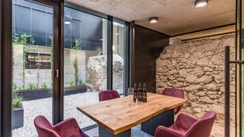 A modern dining area with a wooden table and four chairs, a stone wall, and a view of an outdoor garden through large glass doors.