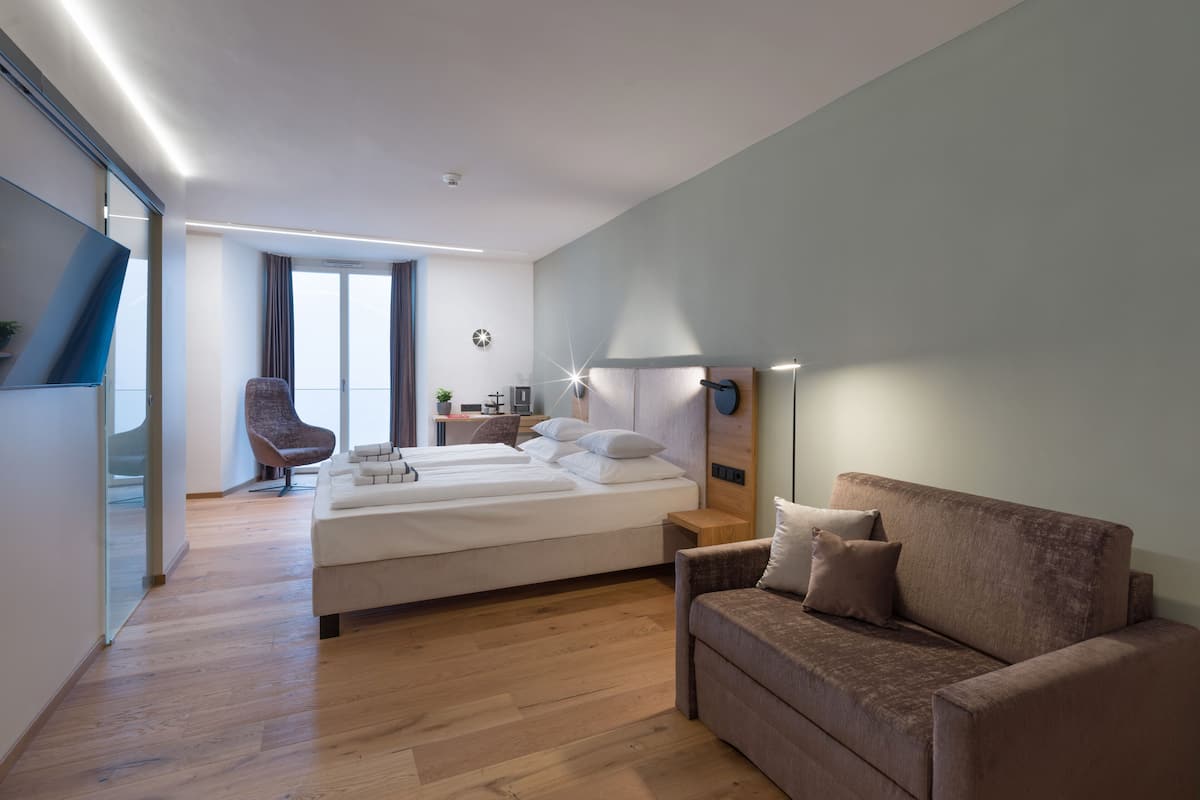 A modern hotel room with a bed, a sofa, a desk, and a chair.