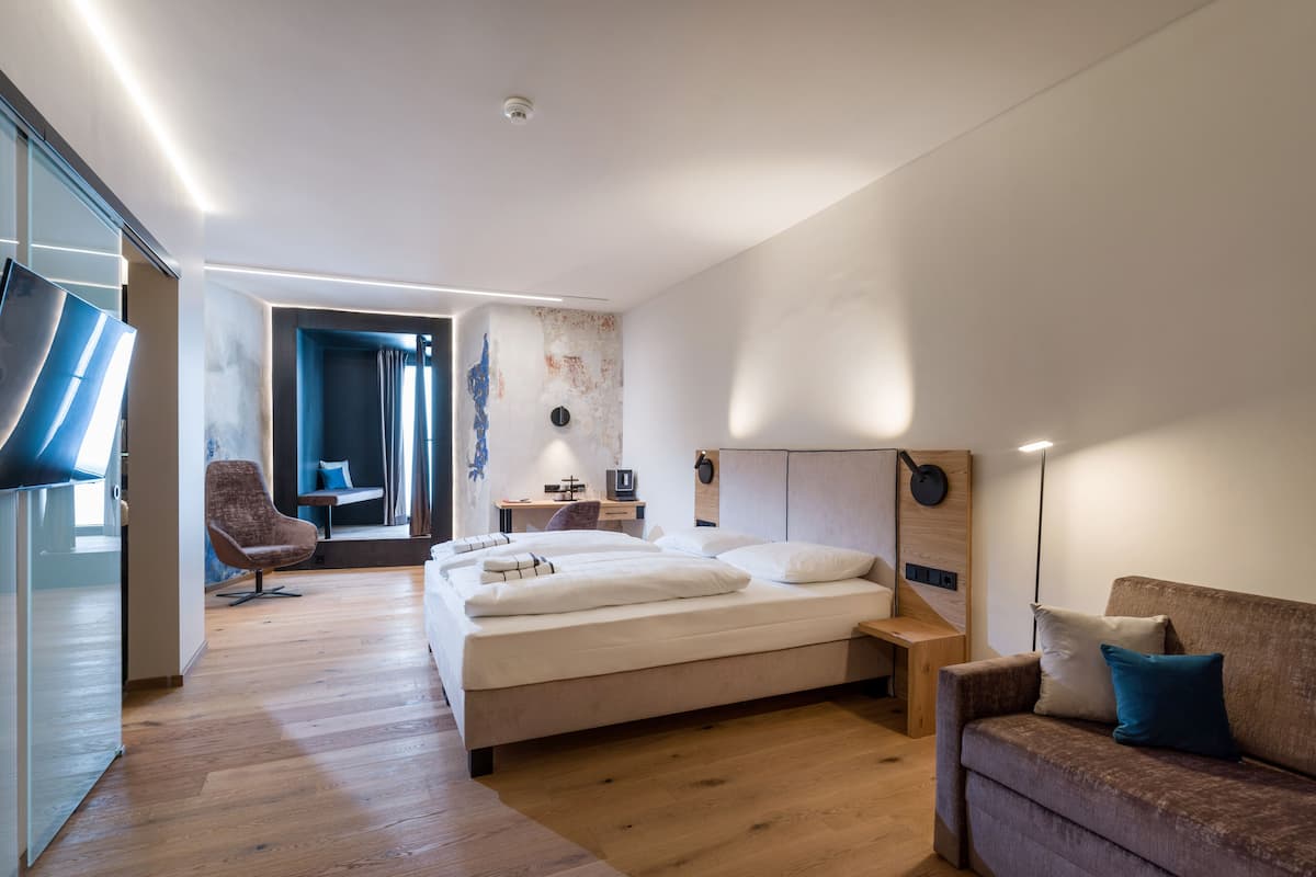 A modern bedroom with a large bed, a desk, a chair, and a sofa.