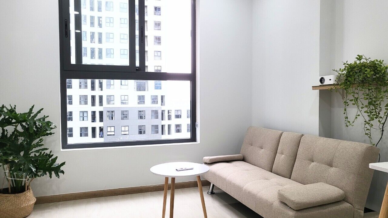 Una sala de estar moderna con un sofá color crema, una mesita blanca y un ventanal con vistas a edificios.