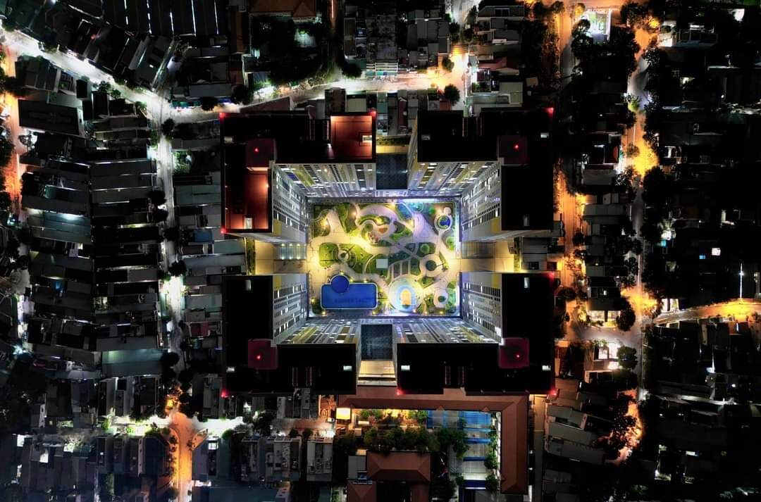 Eine Vogelperspektive auf ein dicht bebautes Stadtgebiet mit einem zentralen Platz, der ein modernes Gebäude mit einem markanten, kreisförmigen Design und einem blauen Sitzbereich zeigt.