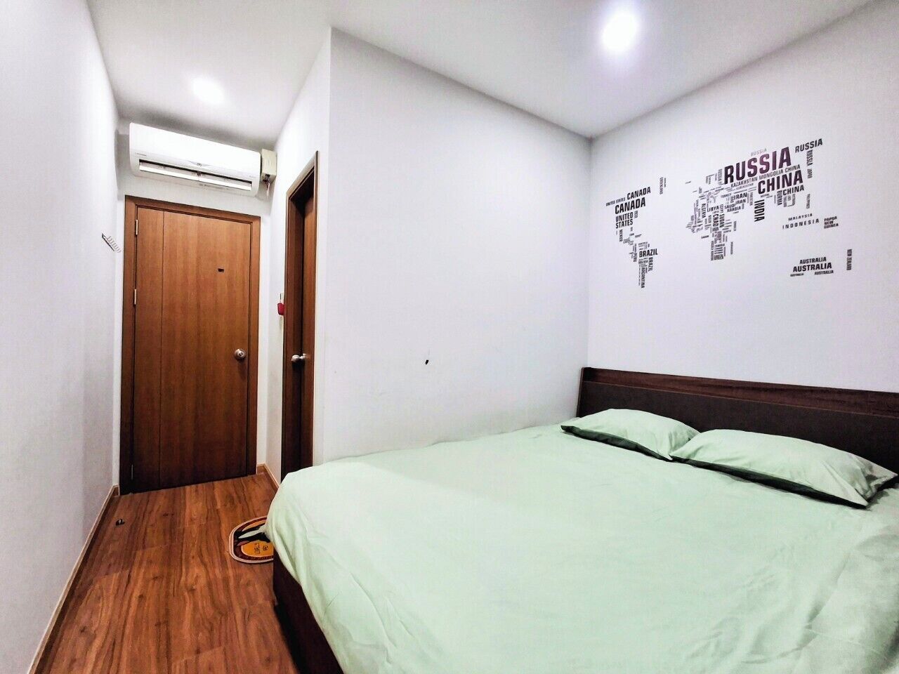 Une chambre avec un plancher en bois, un lit avec une literie verte, une porte en bois et un mur décoré d’une carte du monde.