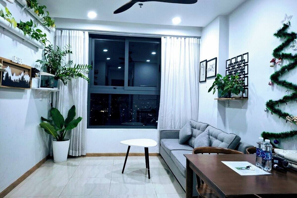 Un salon moderne avec un canapé gris, une petite table ronde, un ventilateur de plafond et une grande fenêtre avec des rideaux.