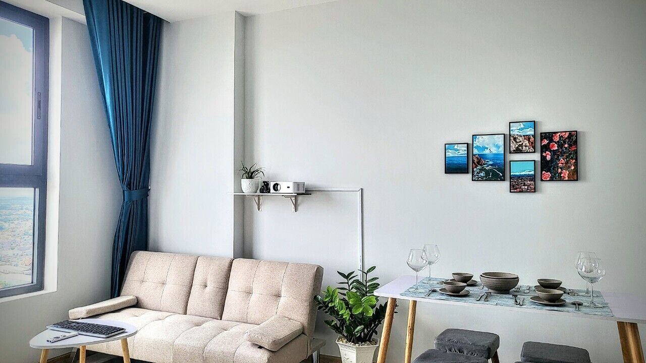 Ein modernes Wohnzimmer mit einer Couch, einem Couchtisch, einem Beistelltisch, einer Pflanze, einem Esstisch mit Geschirr und Gläsern sowie einer Wand mit gerahmten Bildern.