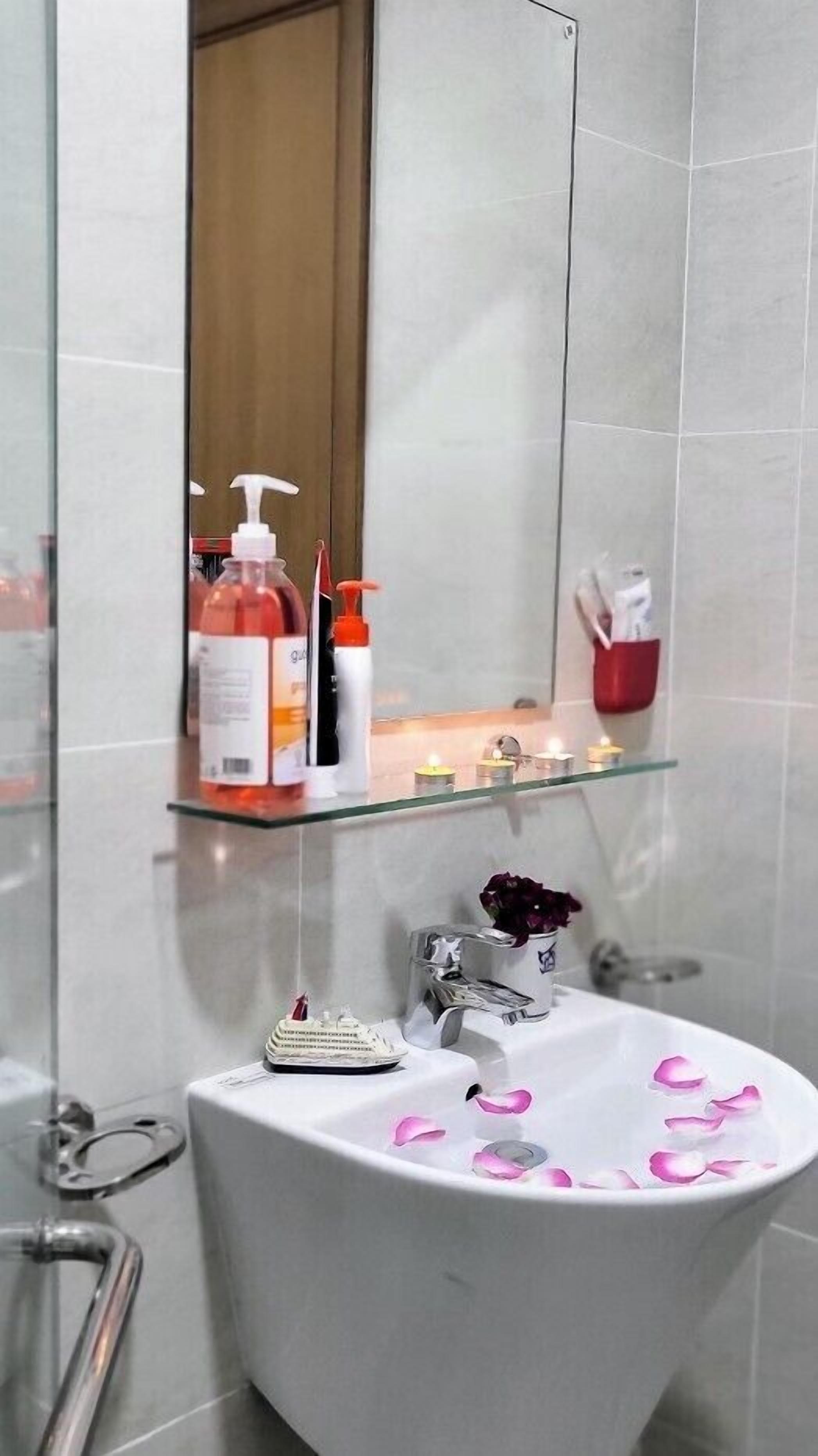 A bathroom with a white sink, a mirror, and toiletries on a shelf.