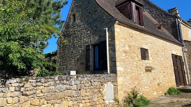 Un edifici de pedra amb teulada inclinada, una xemeneia i una antena satèl·lit.