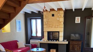Un saló acollidor amb una llar de foc, bigues de fusta, un sofà vermell i una taula de menjador amb sets de taula.