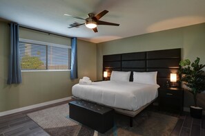 Une chambre à coucher moderne avec un grand lit, un ventilateur de plafond, des lampes de chevet, une table de chevet et une plante en pot.