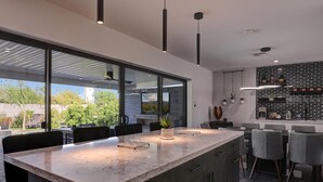 A modern kitchen with a large island, dark cabinetry, and a view of greenery outside. - Gorgeous Scottsdale Home w/ Heated Pool (Scottsdale)