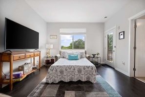 Cozy retreat with a large bed, nightstand, and dresser, plus a flat-screen TV and large window with blinds.