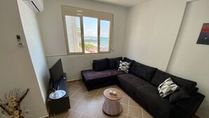 Un salon comprenant un canapé d’angle, un téléviseur, une petite table basse et une fenêtre donnant sur la mer.
