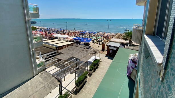 Une vue sur la plage depuis un balcon donnant sur une plage animée, parsemée de parasols et de chaises longues.