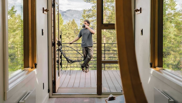 Ein modernes Interieur mit einer großen Glasdoor, die zu einem Balkon, einer Holzterrasse und einer Bergblick führt.