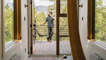 A modern interior with a large glass door leading to a balcony, a wooden deck, and a view of mountains.