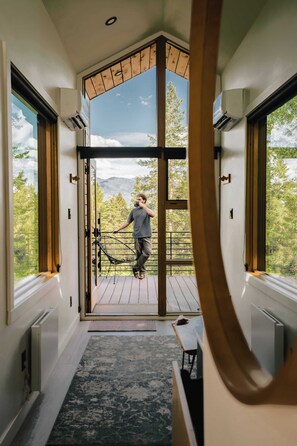A modern interior with a large glass door leading to a balcony, a wooden deck, and a view of mountains.