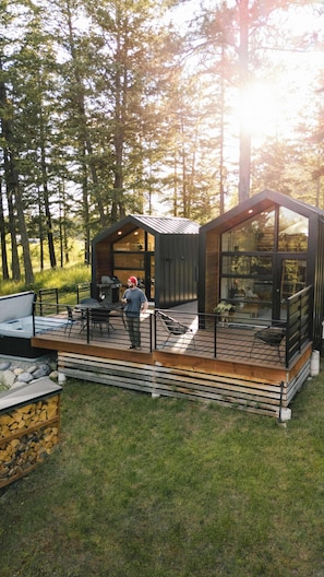 A modern cabin with a deck, outdoor seating, and a grill area.