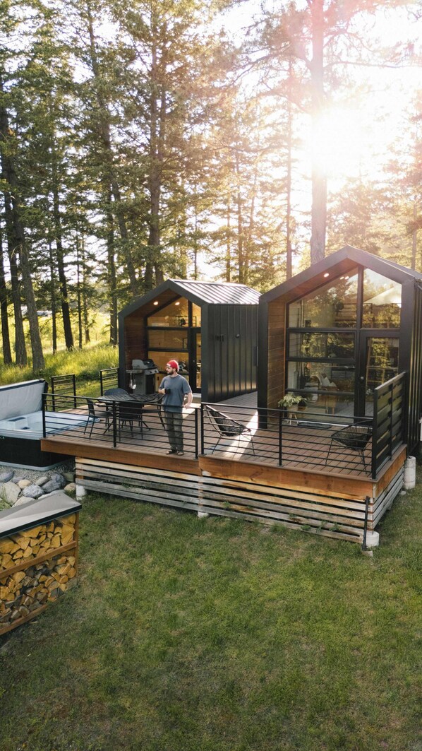 A modern cabin with a deck, outdoor seating, and a grill area.
