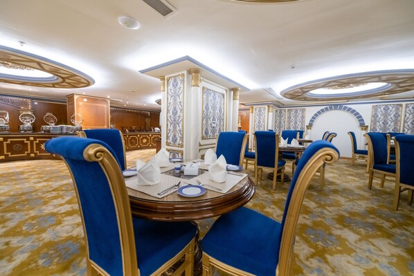 A dining area with round tables, blue upholstered chairs, and a marble-patterned wall.